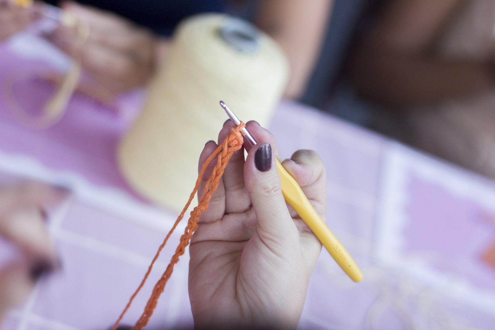 Mãos fazendo crochê com linha laranja durante o encontro
