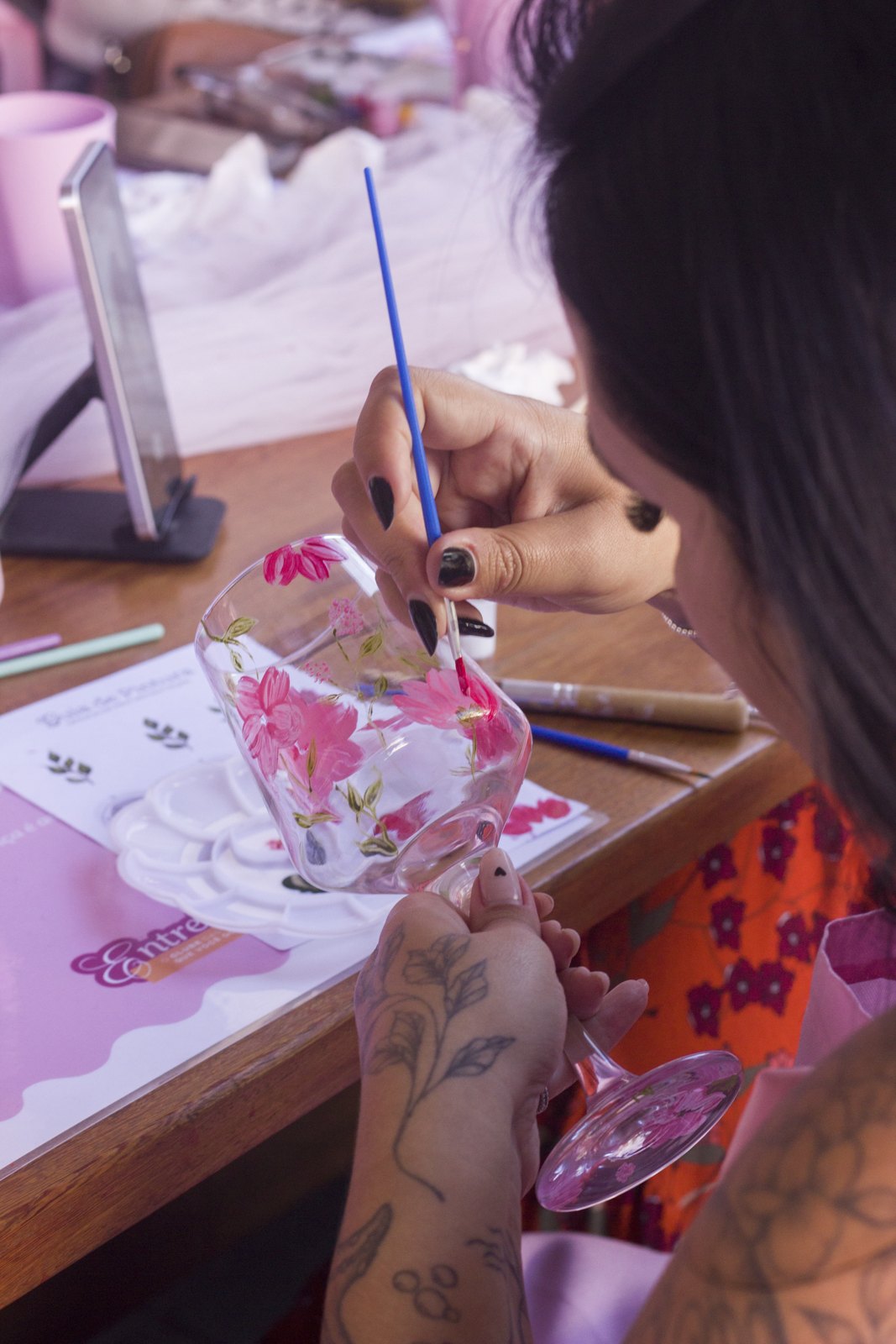 Mãos pintando flores em uma taça de vidro durante a oficina